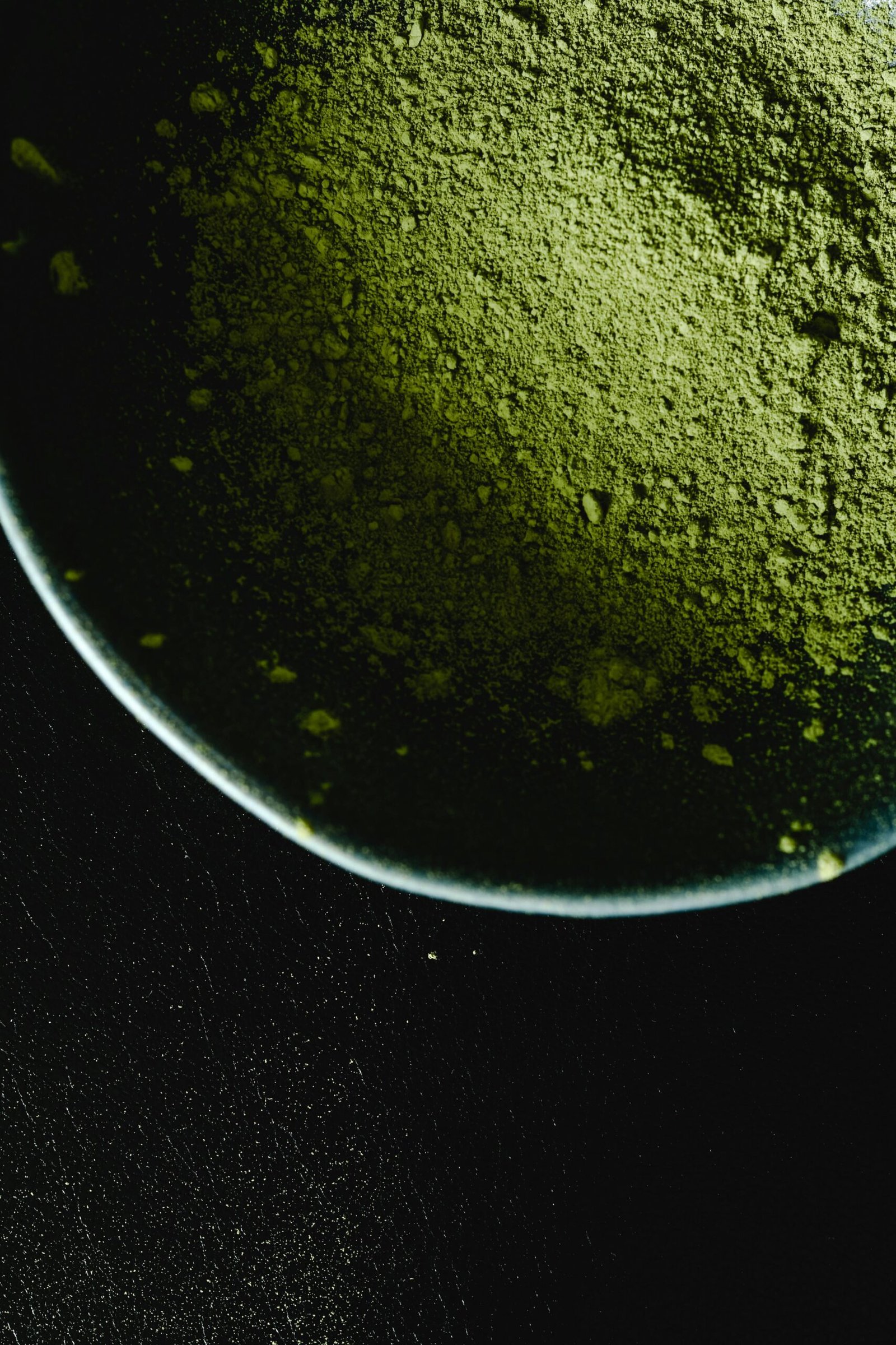 Intriguing close-up of matcha powder in a bowl against a dark background, highlighting texture.